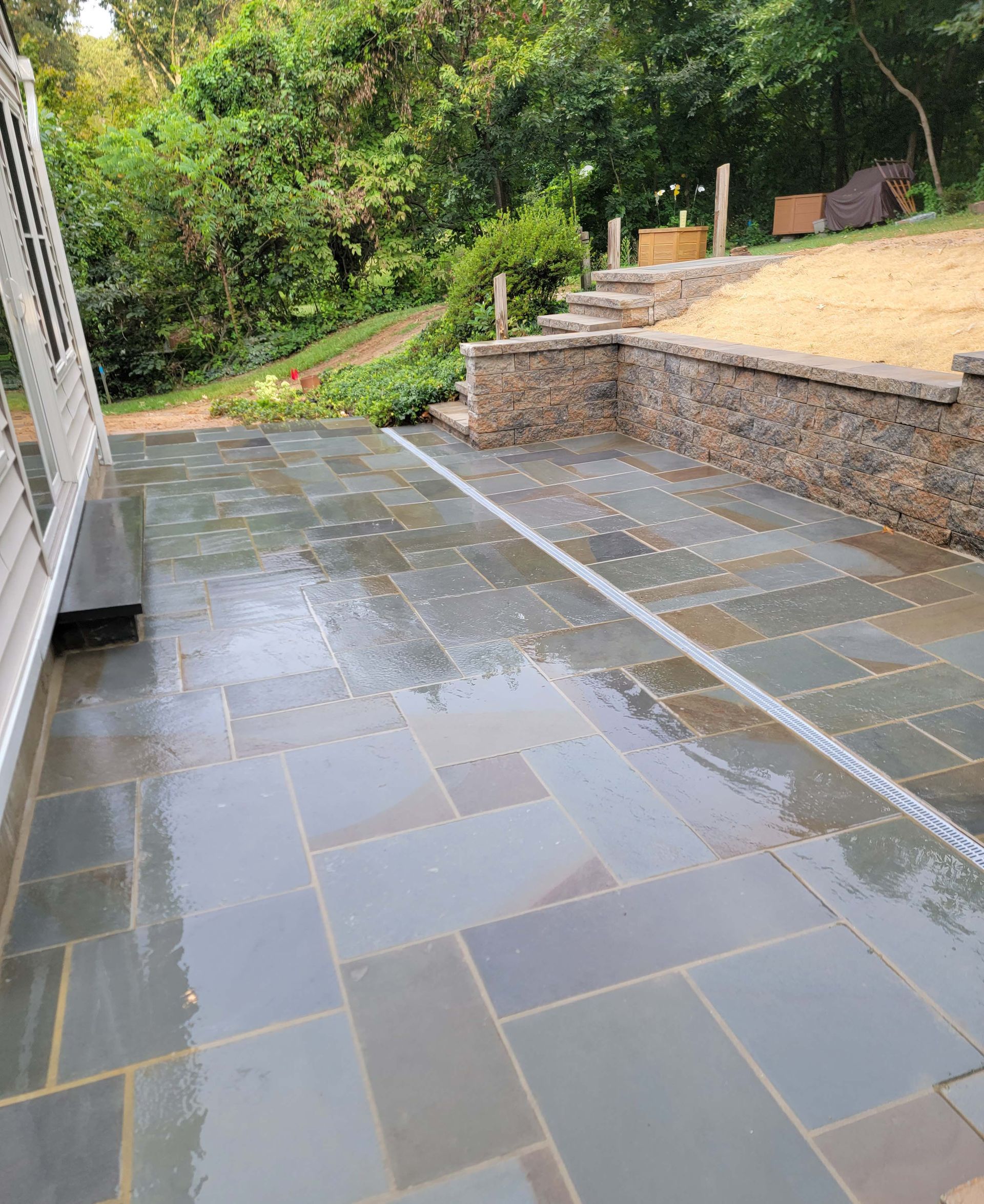 a patio with a stone wall and stairs in the background .