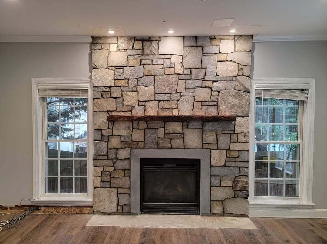 a living room with a stone fireplace and two windows .