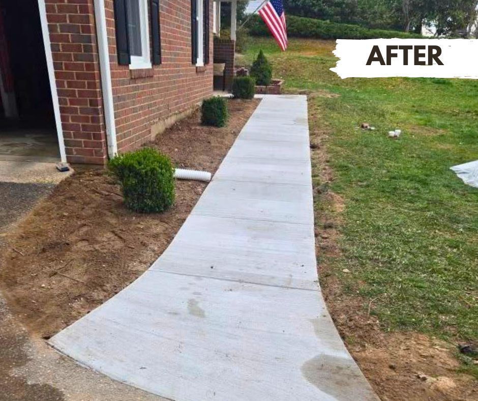 Newly poured concrete walkway curving towards a brick house, surrounded by recently tilled soil with small shrubs and grass.