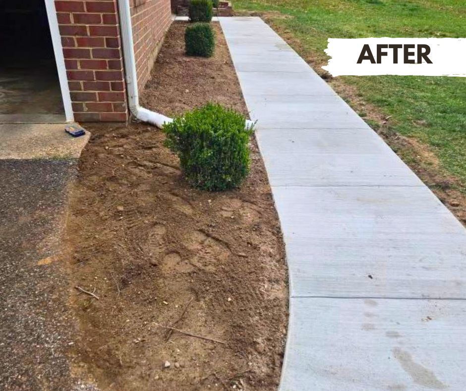 A newly installed concrete walkway beside a brick building. Dirt and bushes are alongside the path.