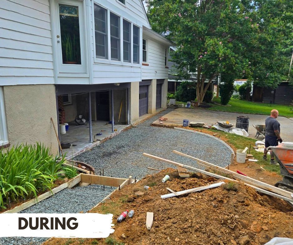 Construction during a home renovation. A gravel pathway is being created alongside a white house, with a worker nearby.