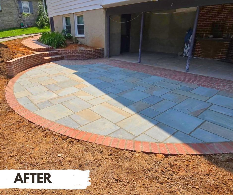 Newly constructed outdoor patio with brick edging and walkway, blue and tan stone tiles, in front of a house with a basement entrance.