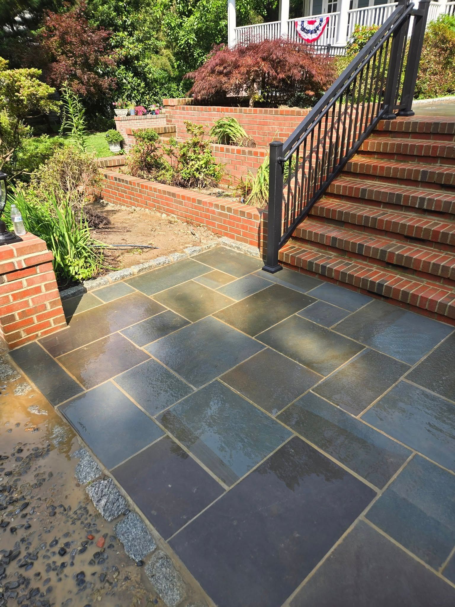 Stone patio and brick steps leading up to a house. A metal railing is on the right.