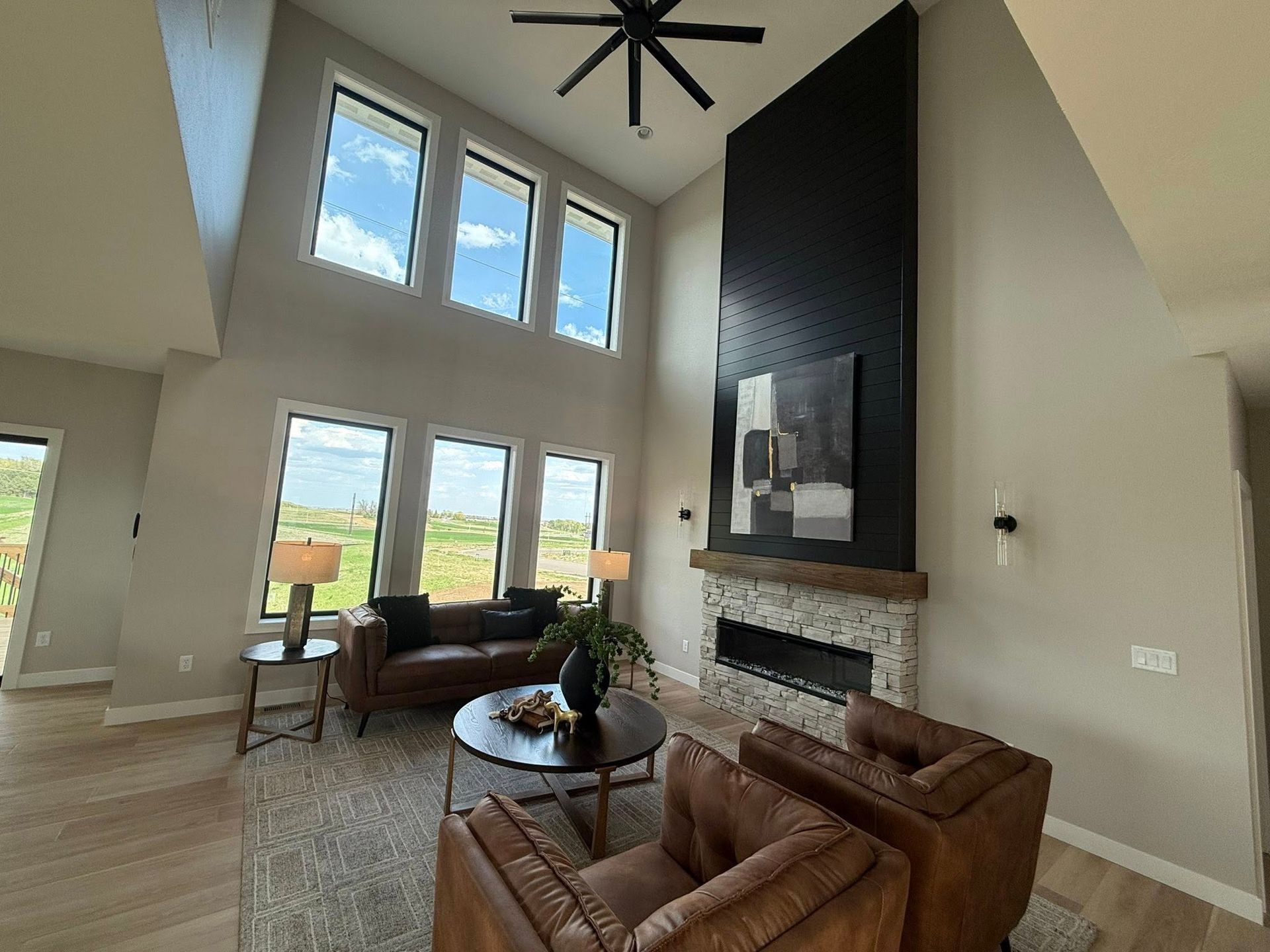 Living room with high ceilings, fireplace, leather furniture, and tall windows.