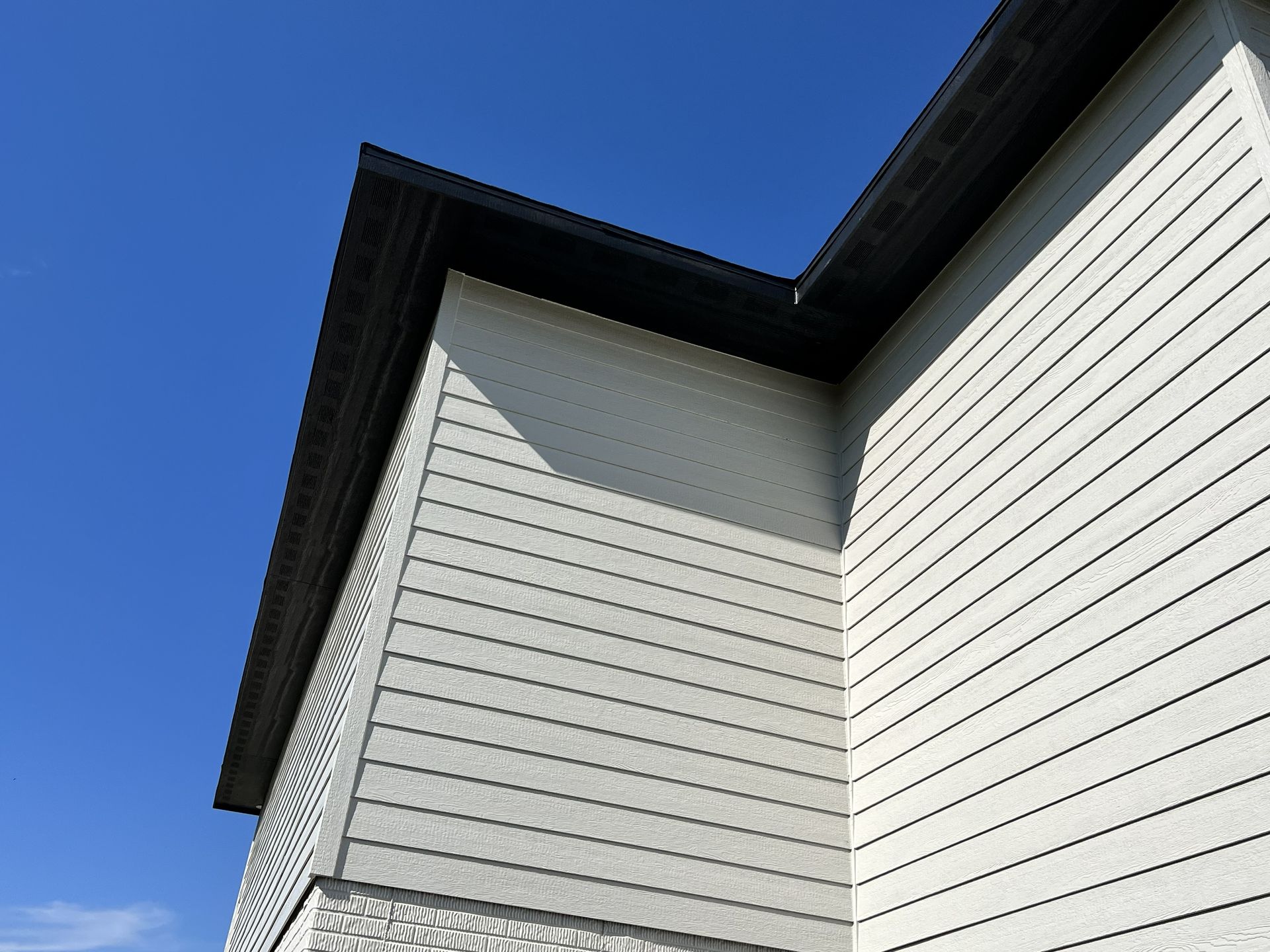 Corner of a house with white siding and dark roof against a clear blue sky.