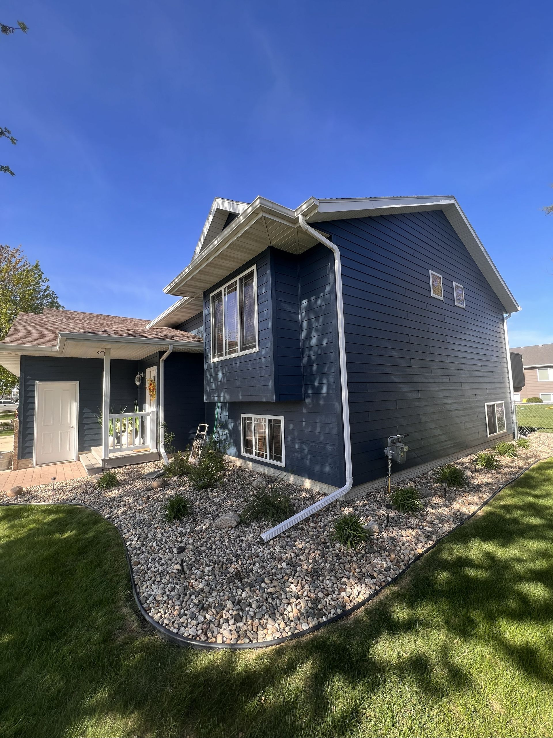 Blue house with white trim and landscaping, under a bright blue sky.