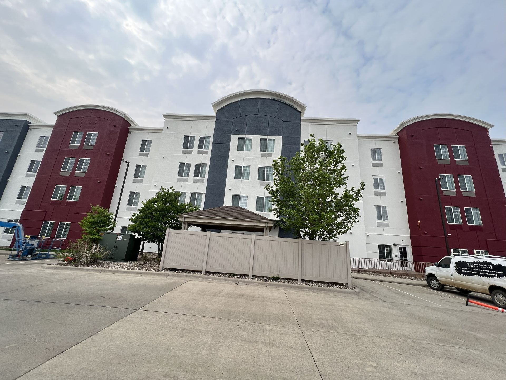 Multi-story building with white, red, and blue facade, windows, and a small fence in front. Overcast sky.
