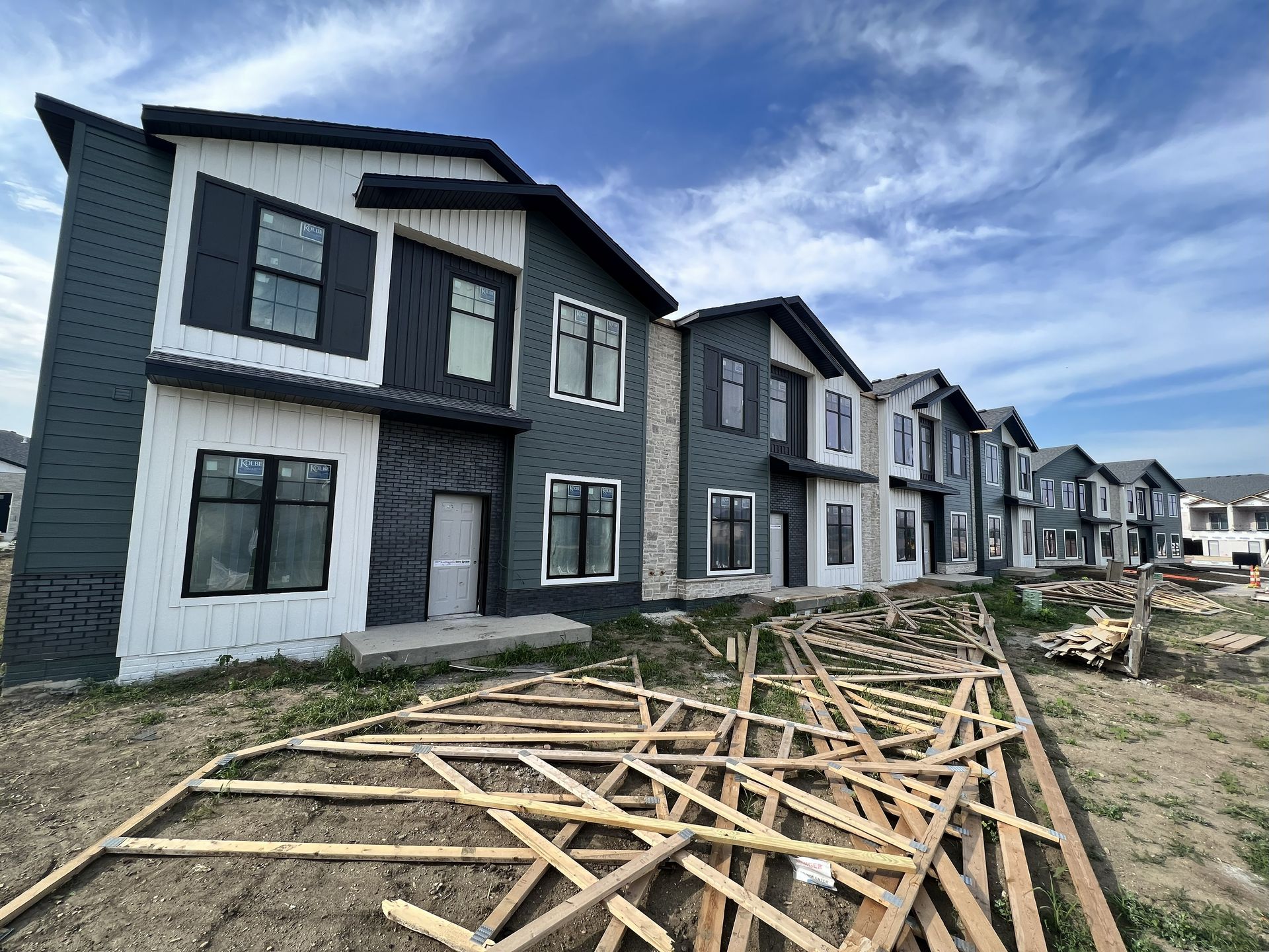 Row of newly constructed townhouses with varying shades of gray and white siding under a cloudy sky, construction debris in foreground.