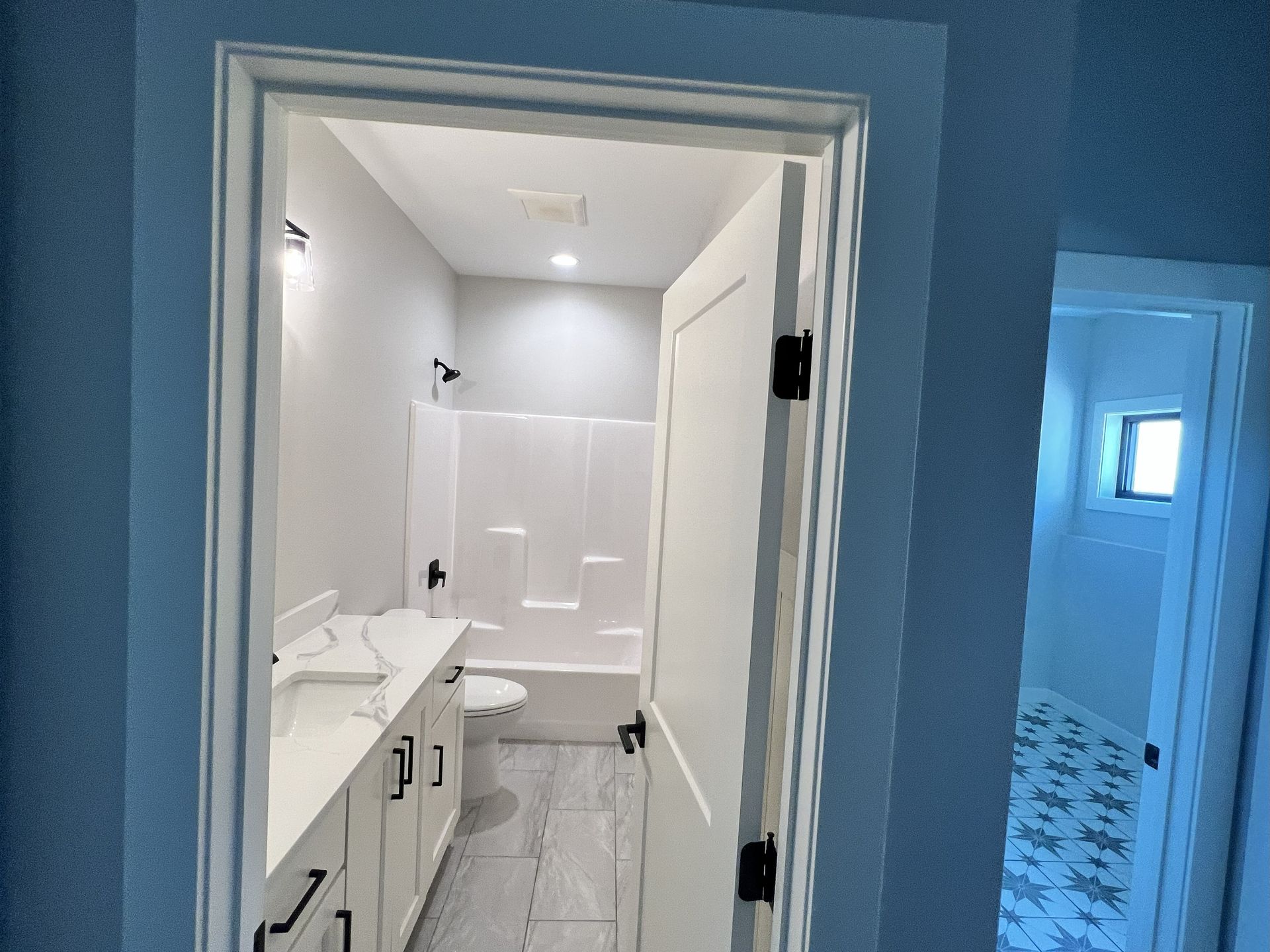Bathroom interior with white vanity, shower/tub, and door. Gray walls and flooring.