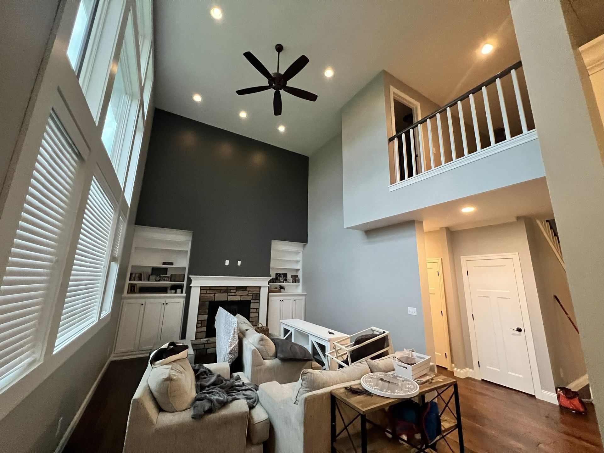 High-ceiling living room with fireplace, built-ins, and a loft, gray walls, white trim, and a dark ceiling fan.