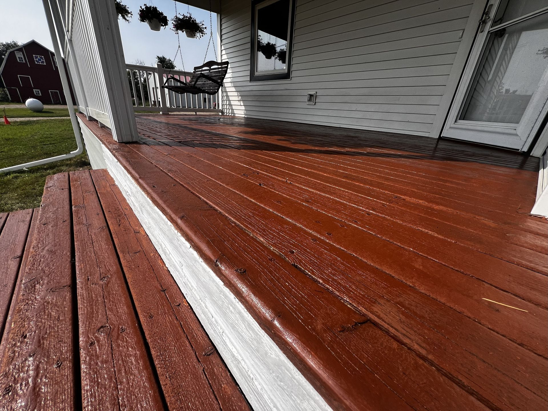 Wooden porch with wet, reddish-brown boards and white trim, leading to a house with a swing.