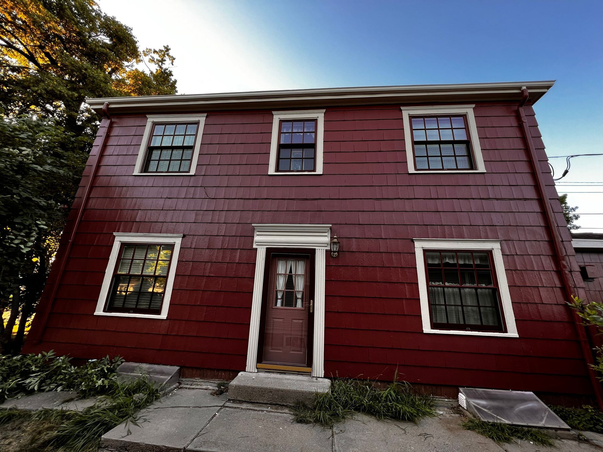 Red two-story house with six windows, a door, and a concrete path.