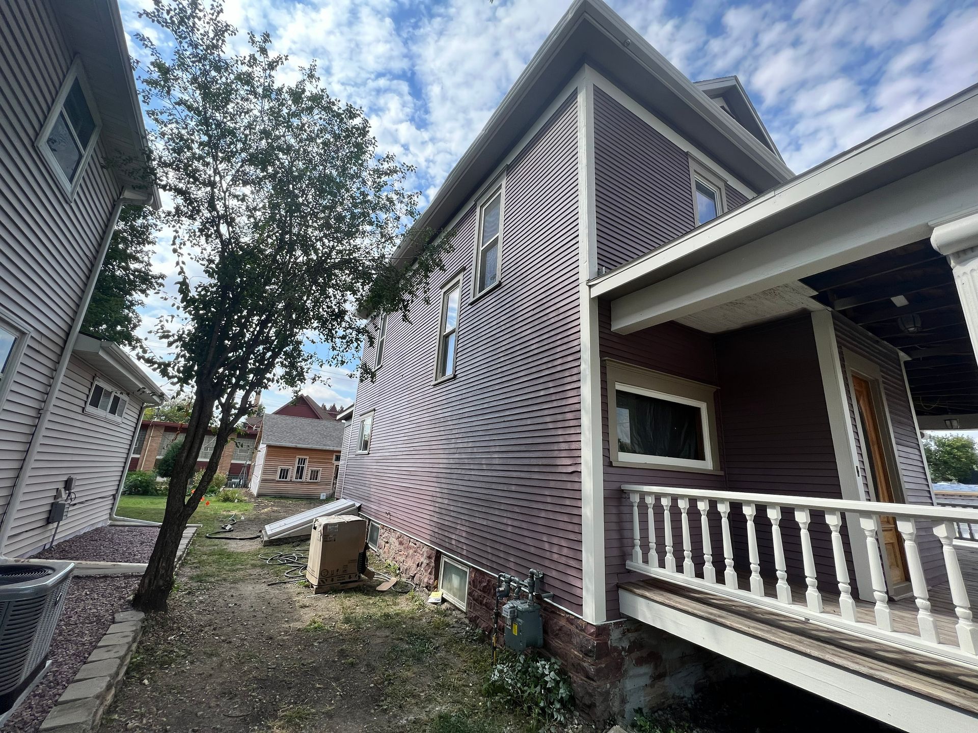 Two-story house with dark red siding, white trim, and a porch. Tree and neighboring house on the left.