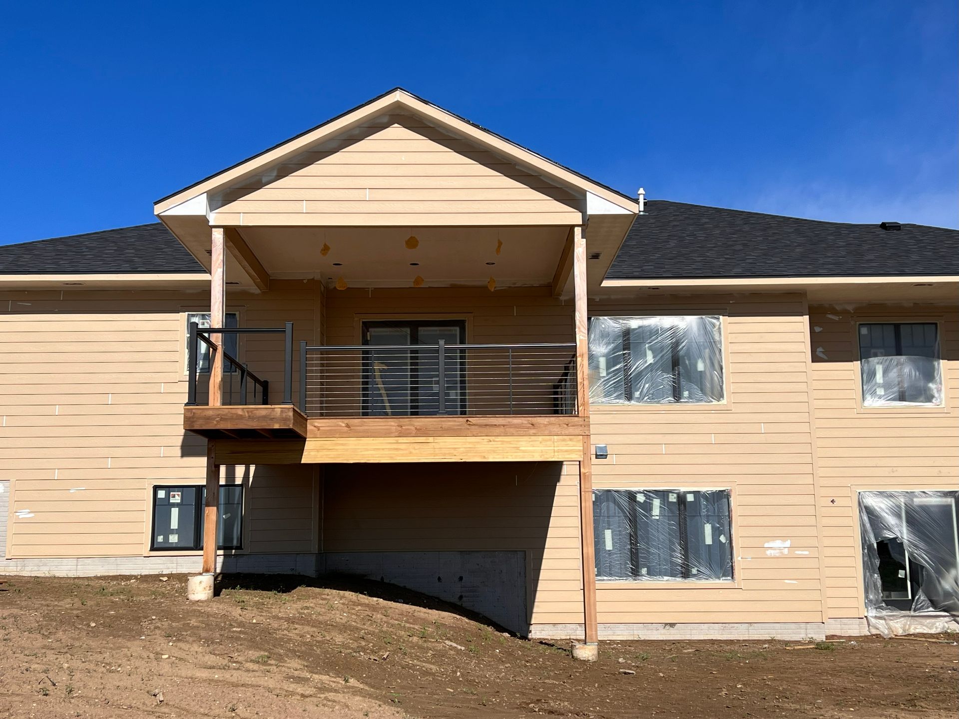 Rear view of a two-story beige house with a deck and covered patio. Windows are covered in plastic.