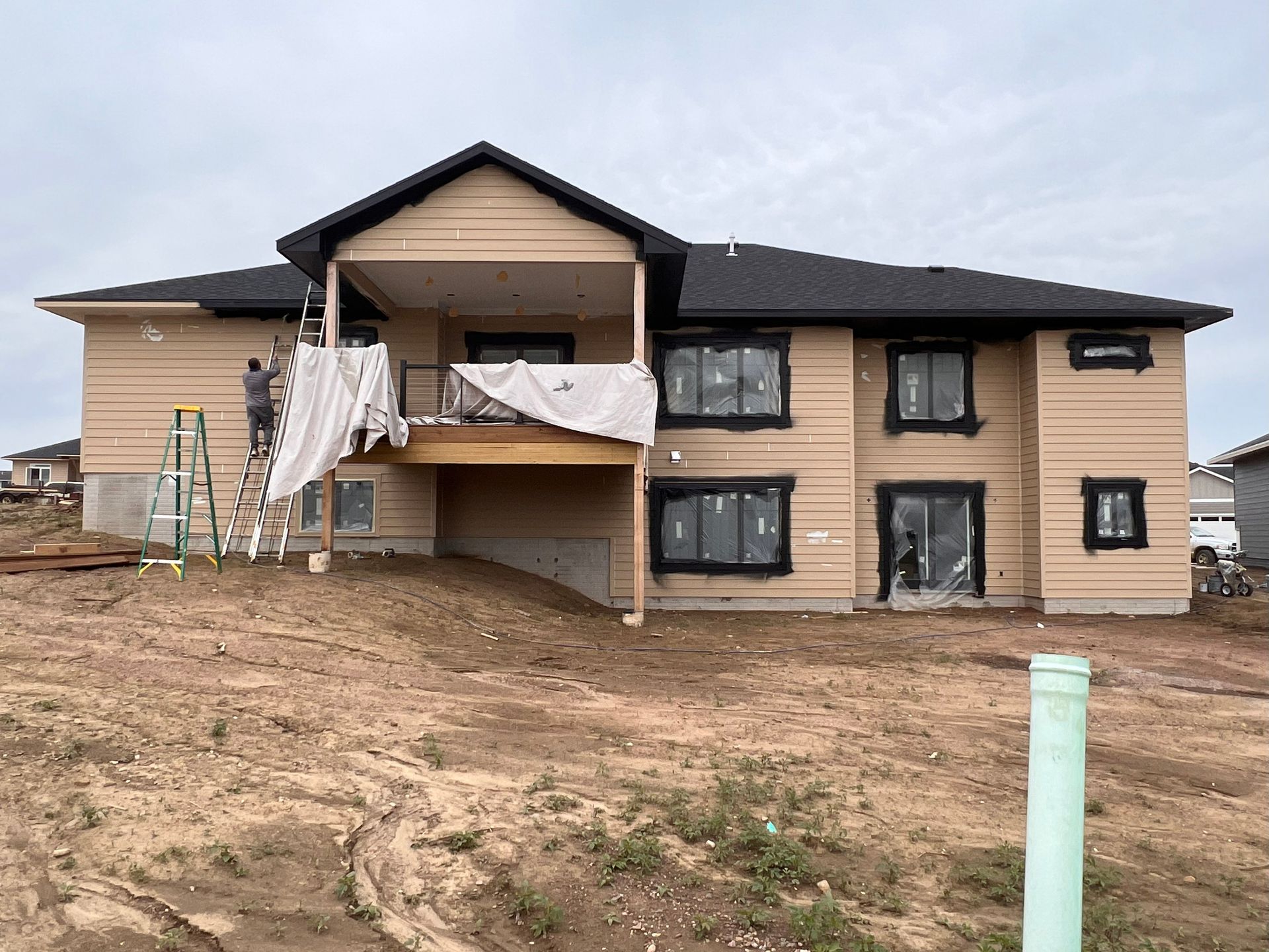 Two-story house under construction, with tan siding, black windows, and a partially covered deck.
