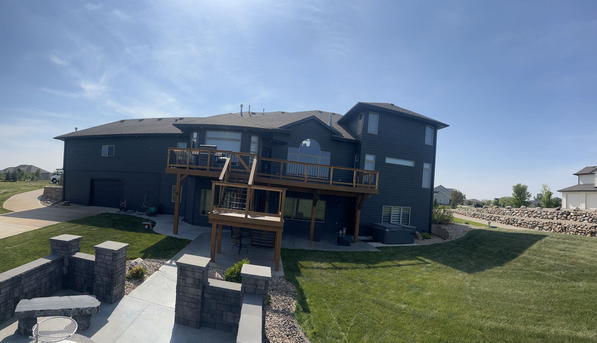 Dark blue house with wooden decks and a driveway, under a blue sky.