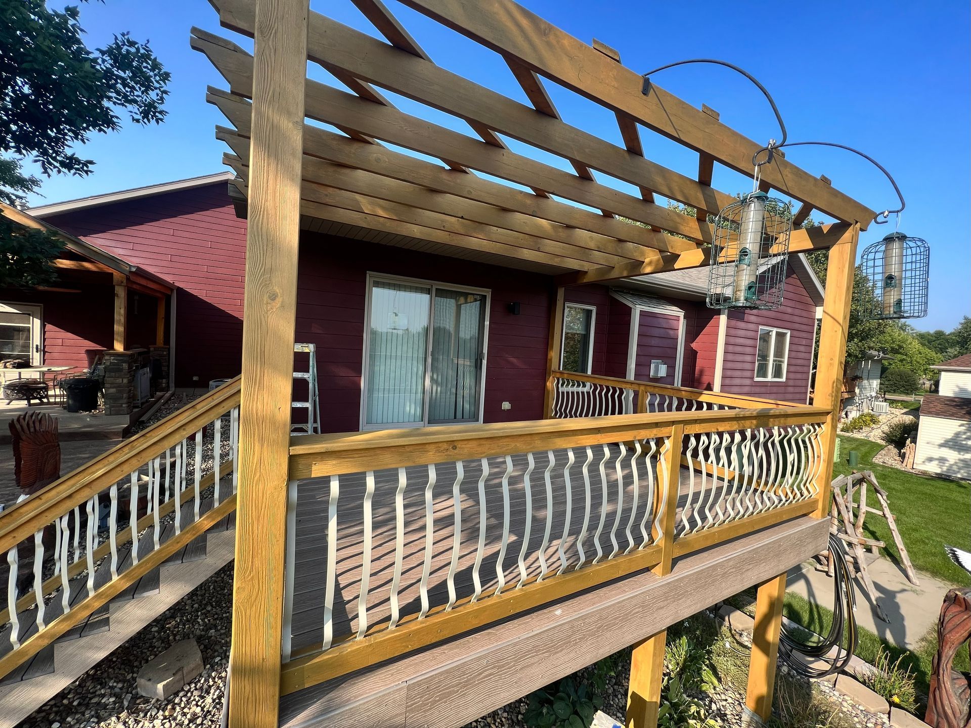 Wooden deck with pergola, stairs, and railing in front of a burgundy house.