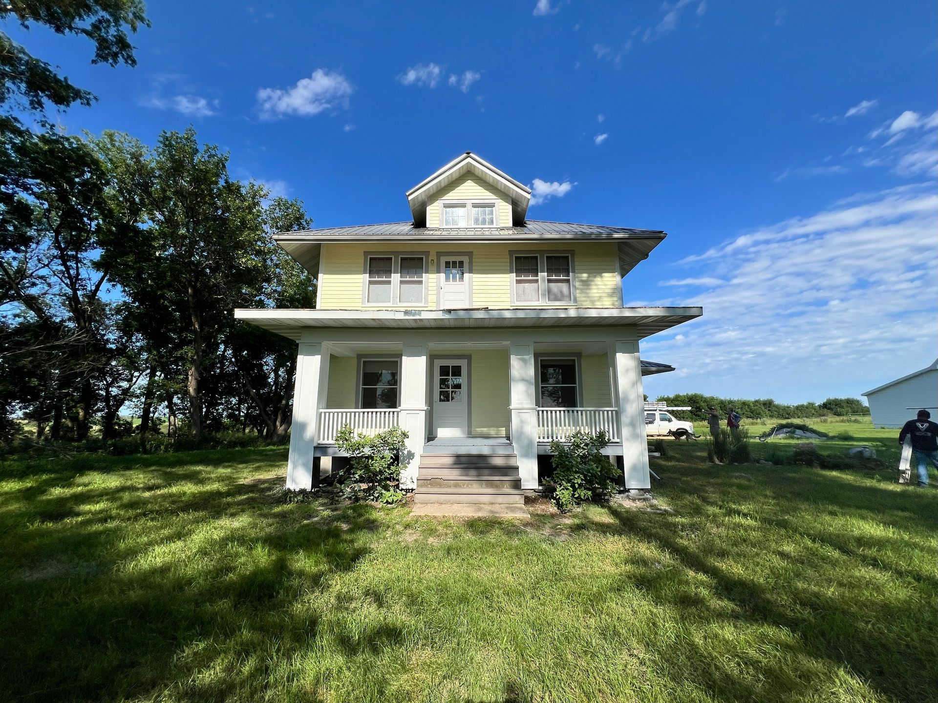 Yellow two-story house with porch and small gable on a grassy lot under a blue sky.