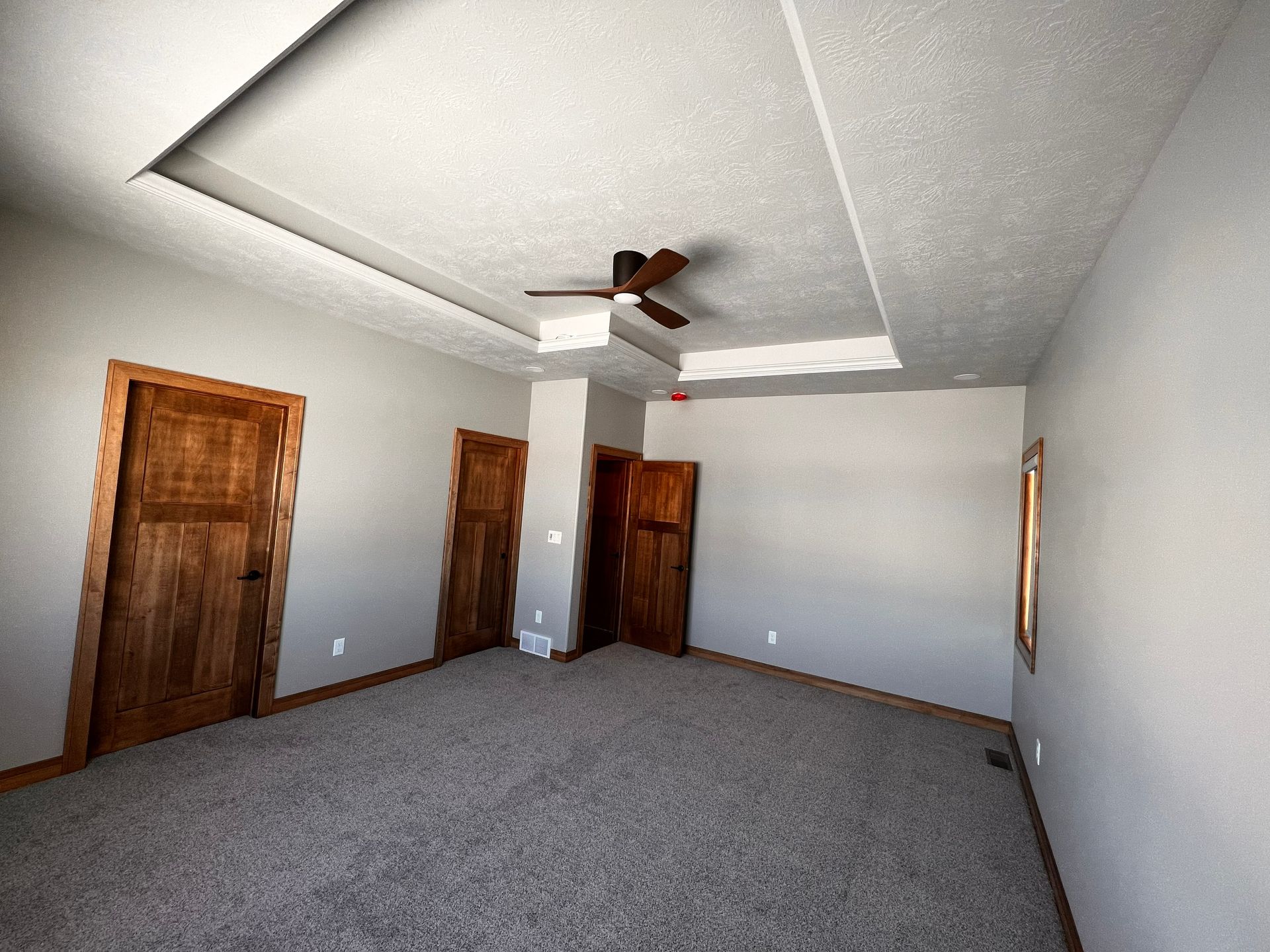 Empty room with carpet, wooden doors, and a ceiling fan, with a recessed ceiling and neutral-colored walls.