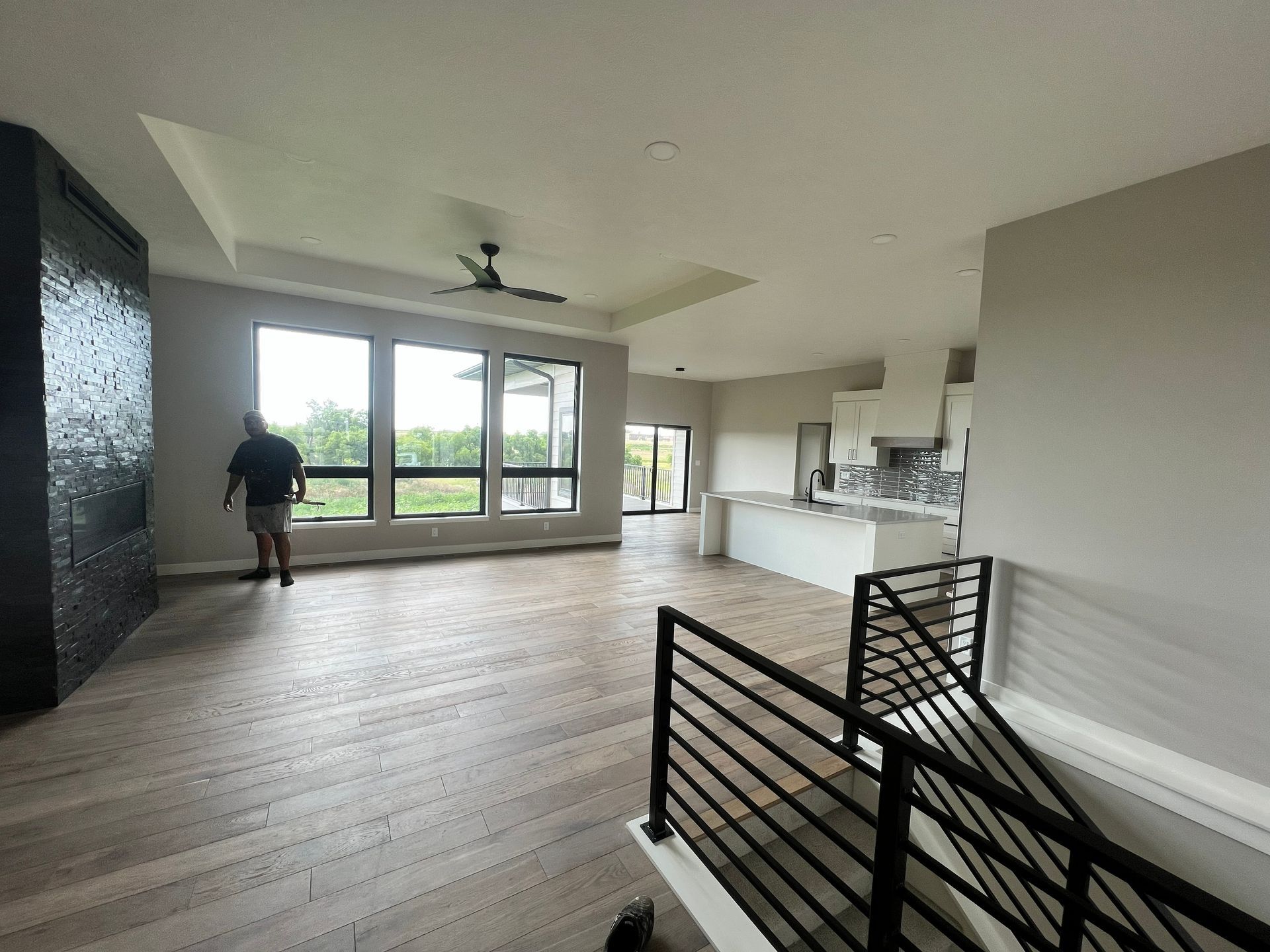 Spacious, open-concept home interior with large windows and a person standing near them. Hardwood floors and modern kitchen.