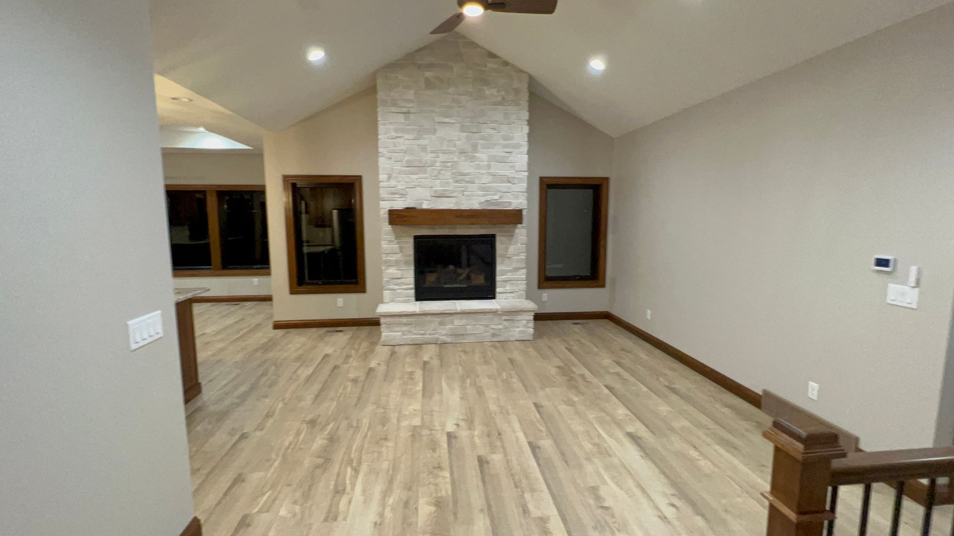 Living room with fireplace and light wood floors. Vaulted ceiling, stone fireplace surround, wooden mantel.