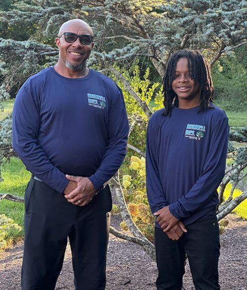 Two people in matching blue shirts posing outdoors in a wooded area
