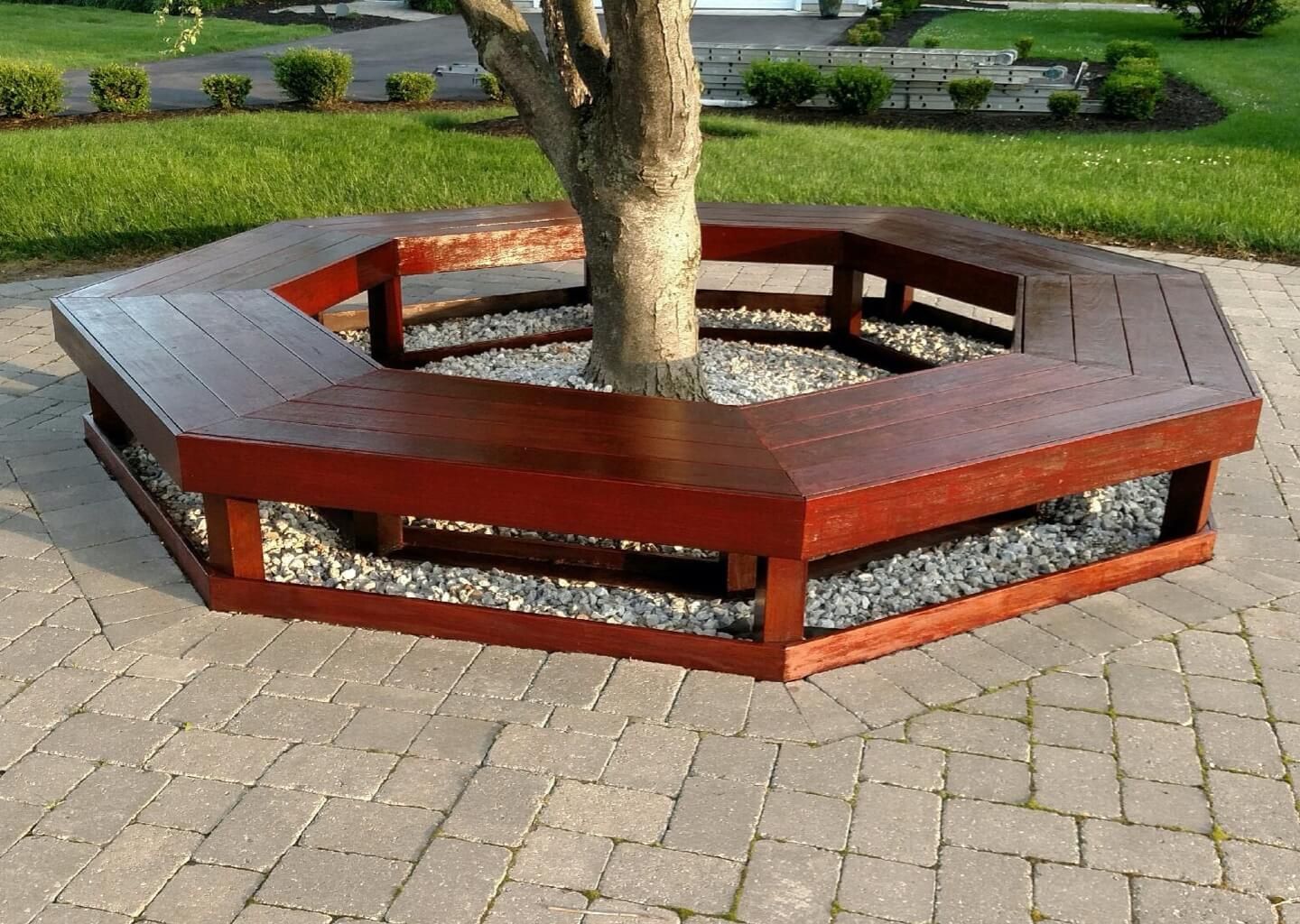 Hexagonal wooden bench encircling a tree in a paved park area
