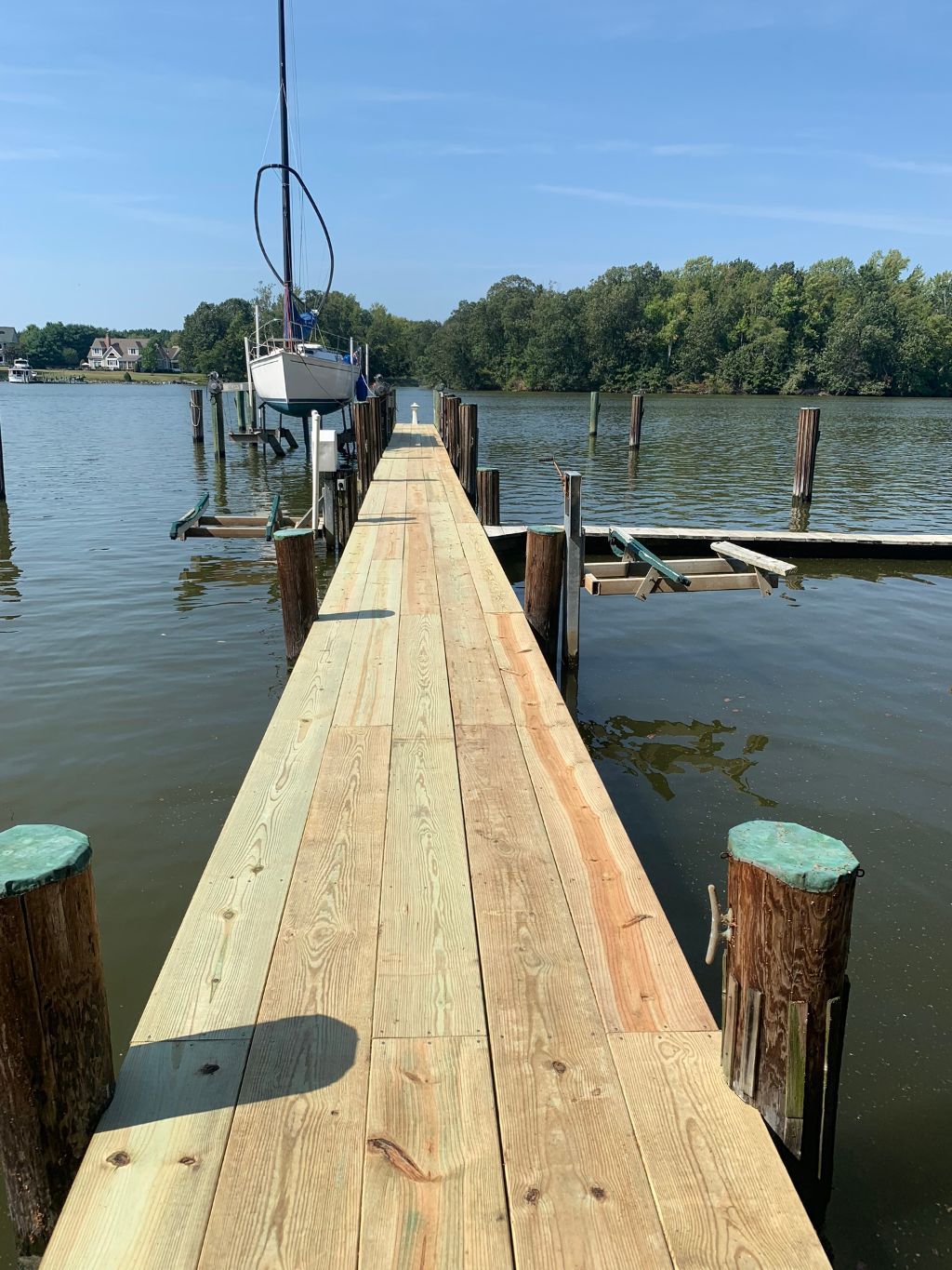 Wooden dock extending over calm water toward trees under a clear blue sky