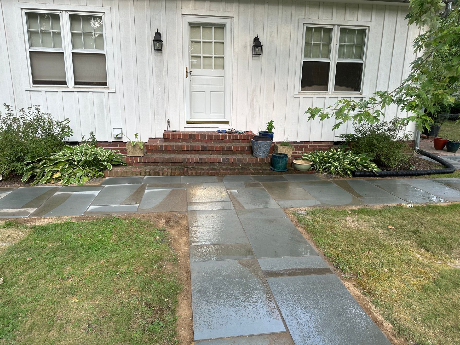 Front walkway leading to a white house with brick steps and potted plants by the entryway
