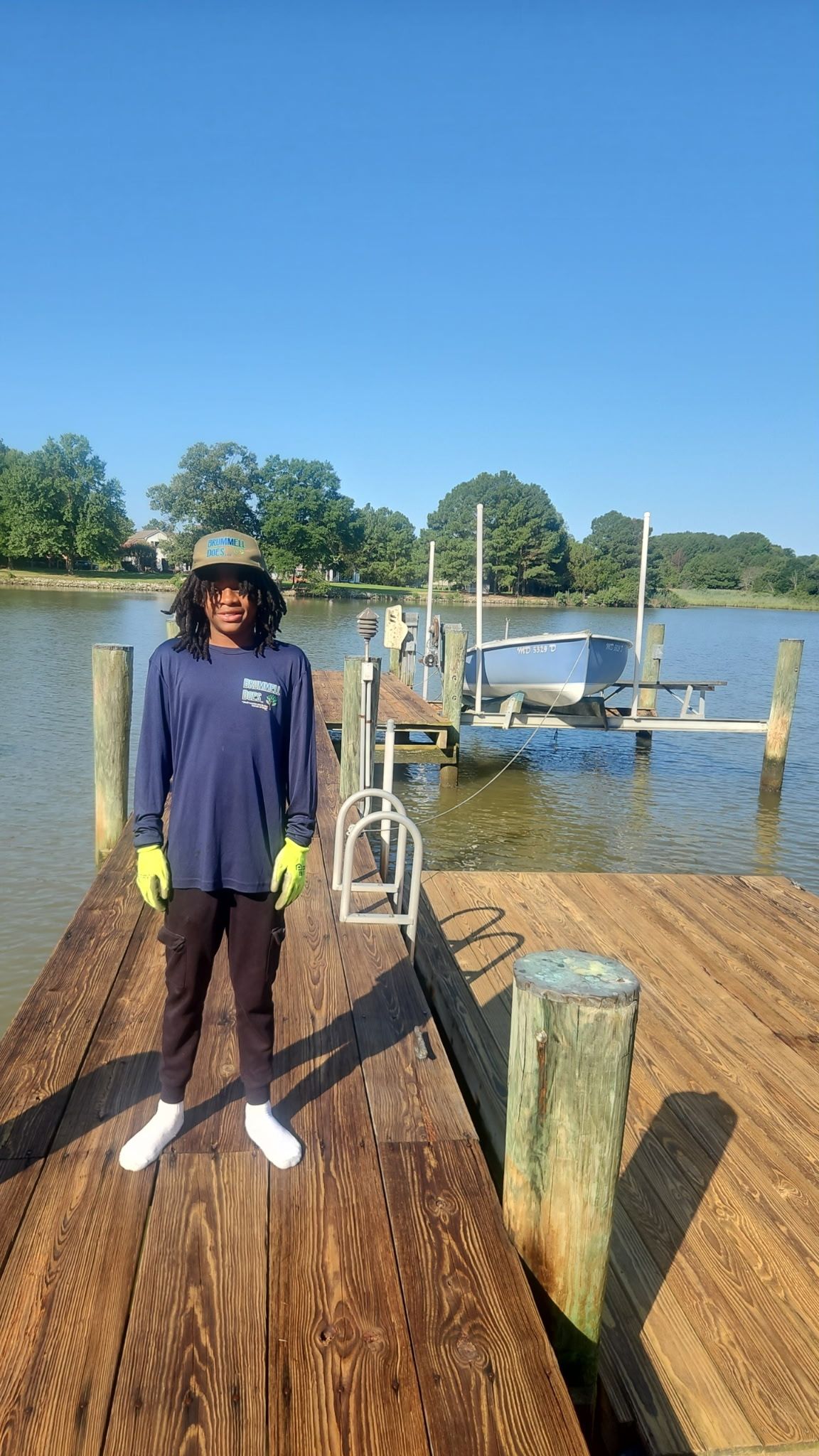 Person standing on a wooden dock by the water, with a bicycle and boats in the background.