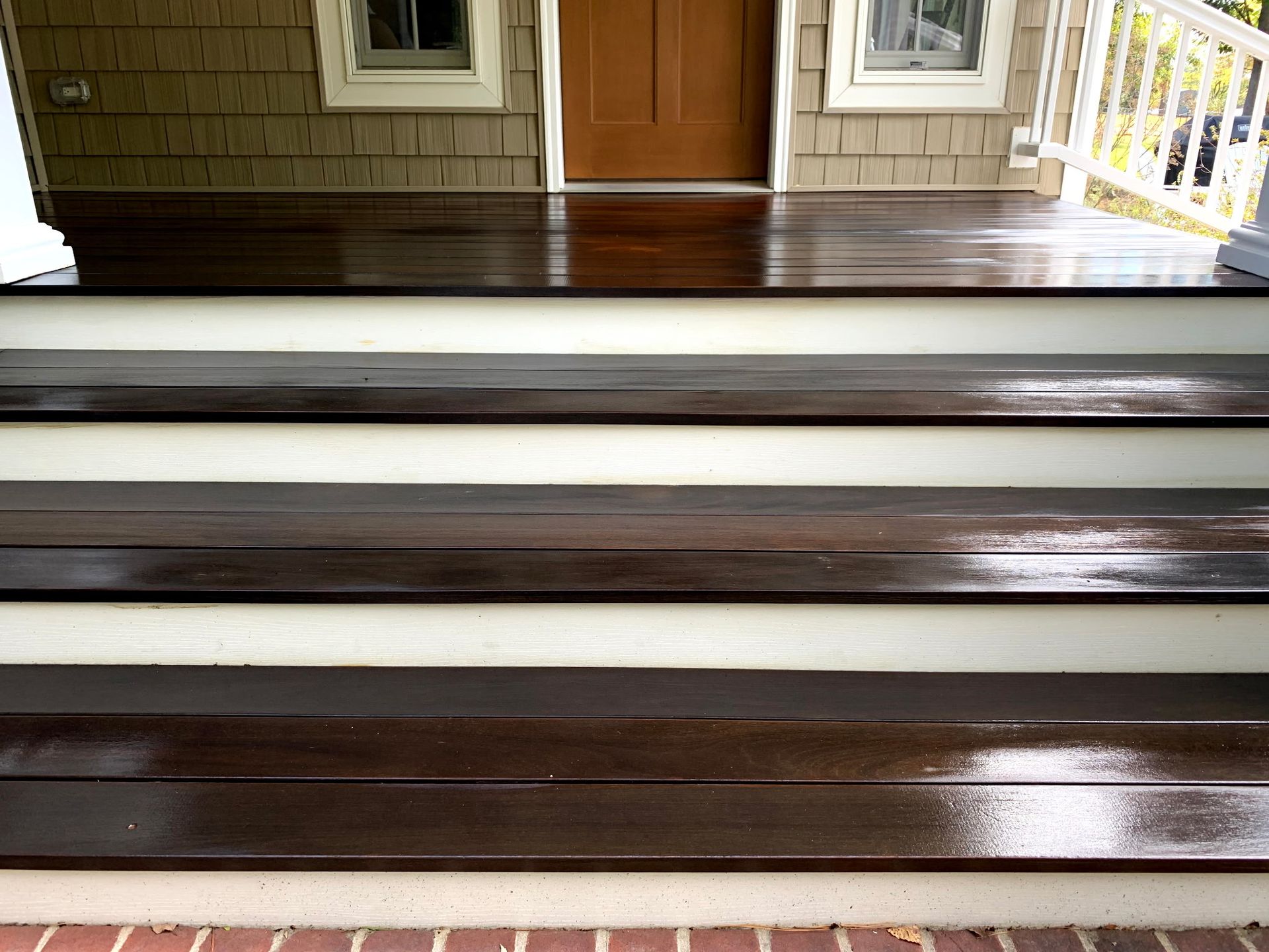 Glossy brown wooden porch steps leading to a front door with white railings on either side