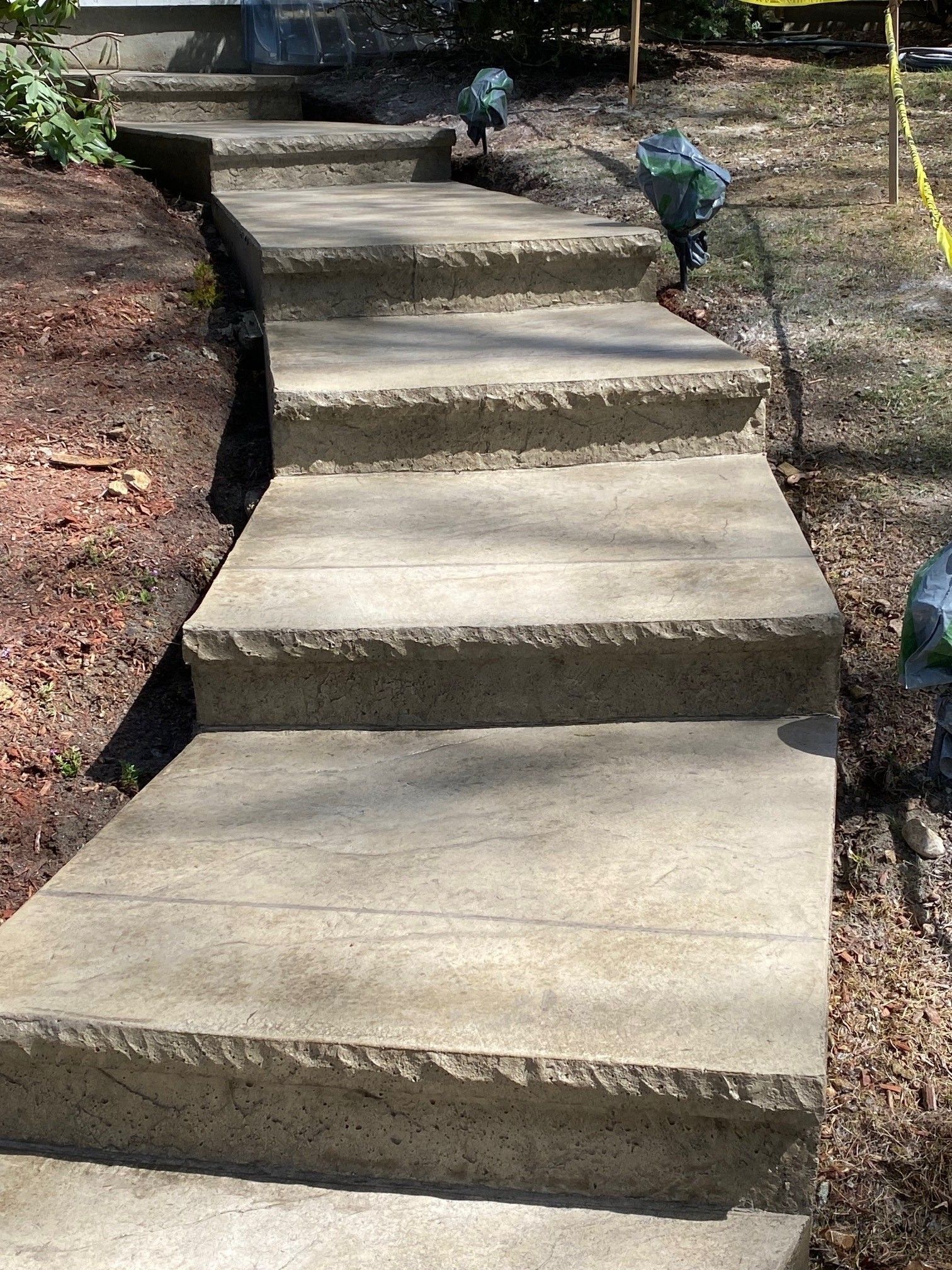 A straight outdoor concrete staircase with textured edges leading upward through a garden setting.