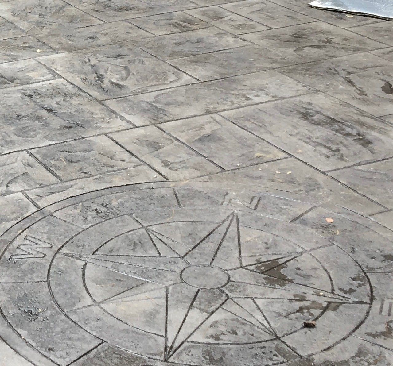 Gray stamped concrete patio floor featuring a circular nautical compass rose design with cardinal directions marked.