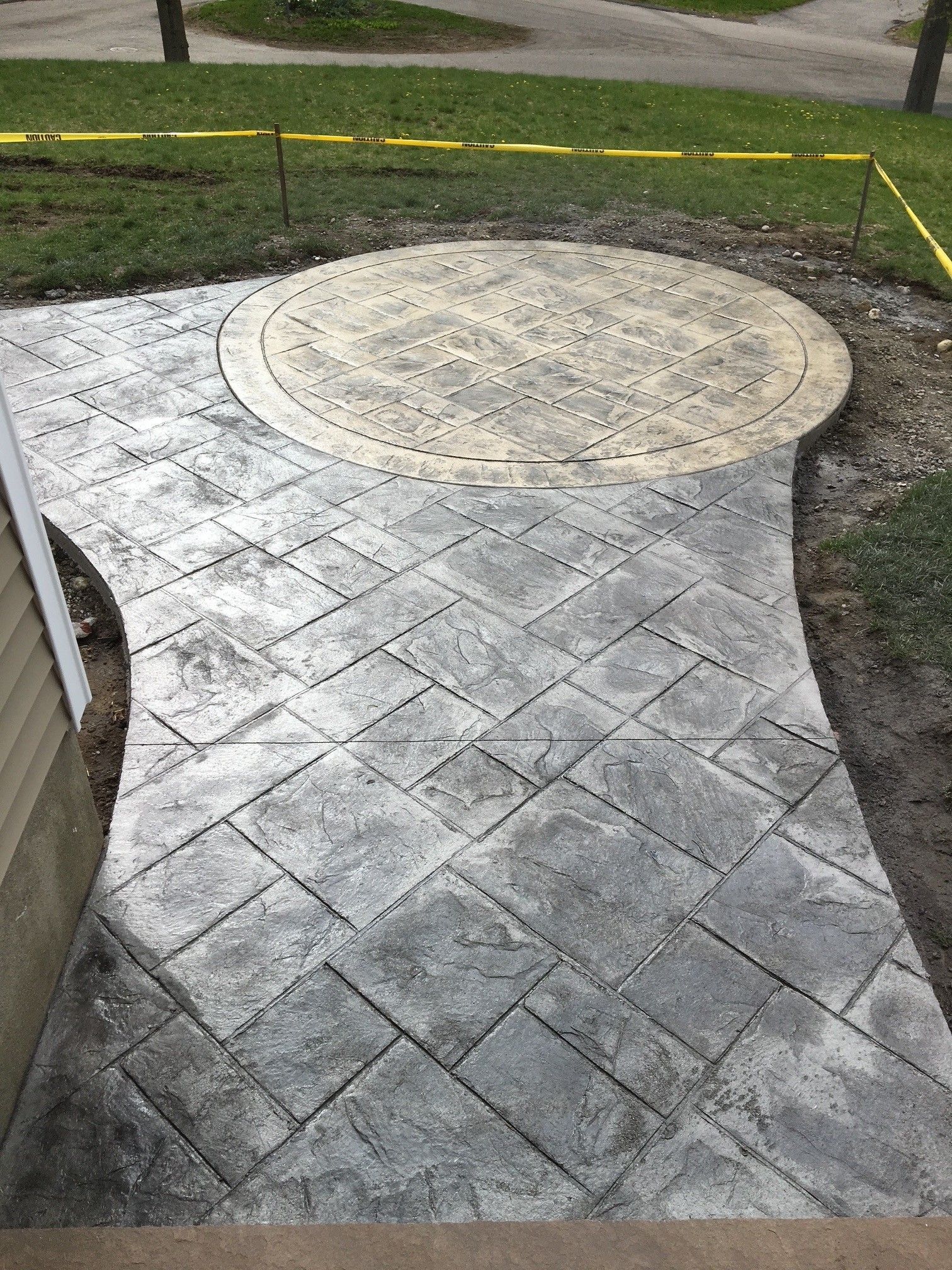 Stamped concrete patio and walkway with a gray stone-patterned path leading to a round, beige circular feature.