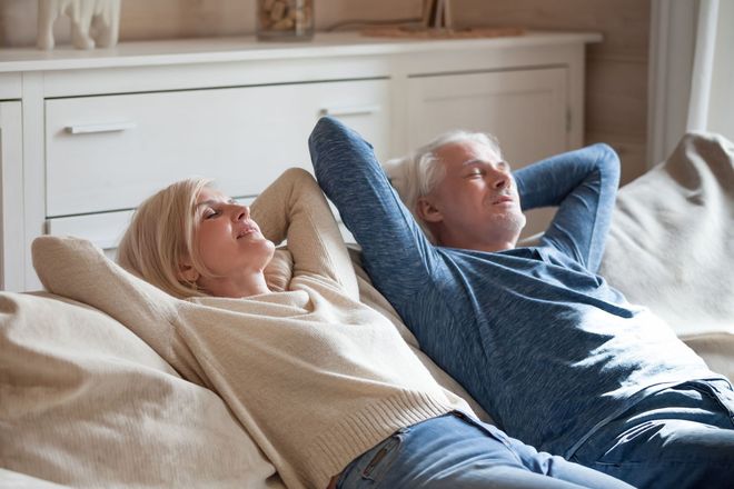 Two people reclining on a couch with hands behind their heads in a sunlit living room