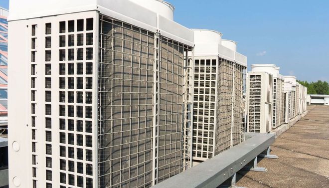 Row of rooftop HVAC units with large fans and white casings along a gravel rooftop