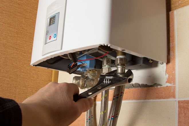 Person tightening a wall-mounted boiler connection with a wrench
