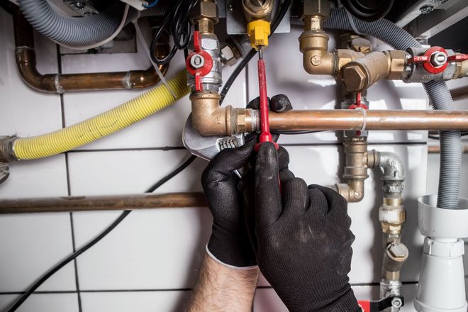 Technician tightening a red valve on exposed plumbing pipes with a wrench