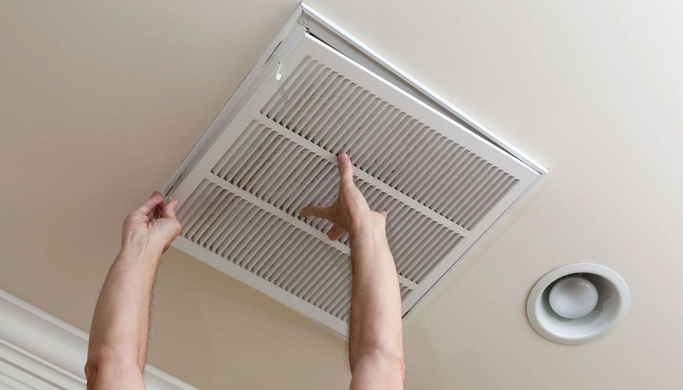 Hands removing a ceiling vent cover next to a recessed light.