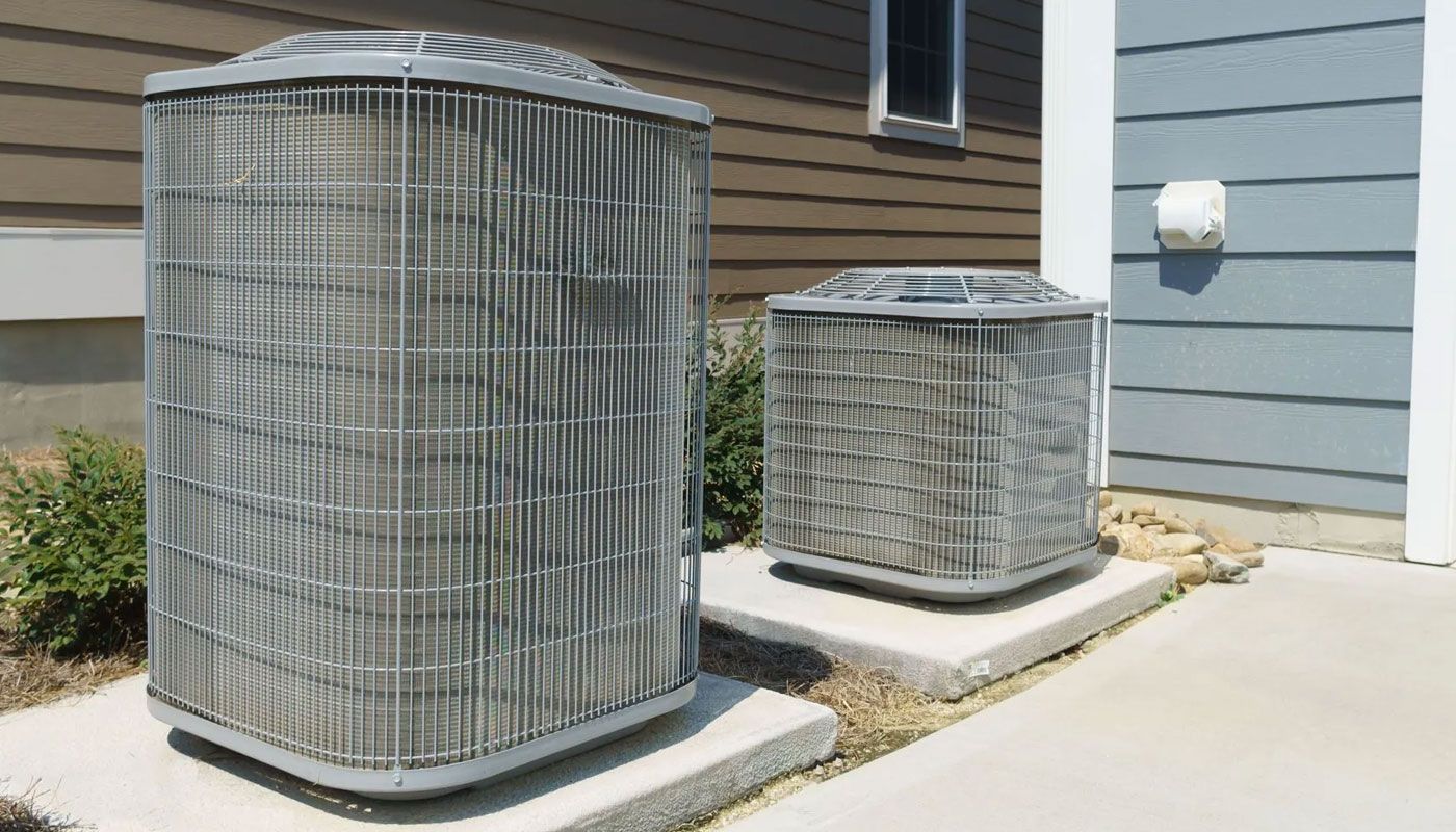 Two outdoor HVAC units beside a building, one large and one small, on concrete pads