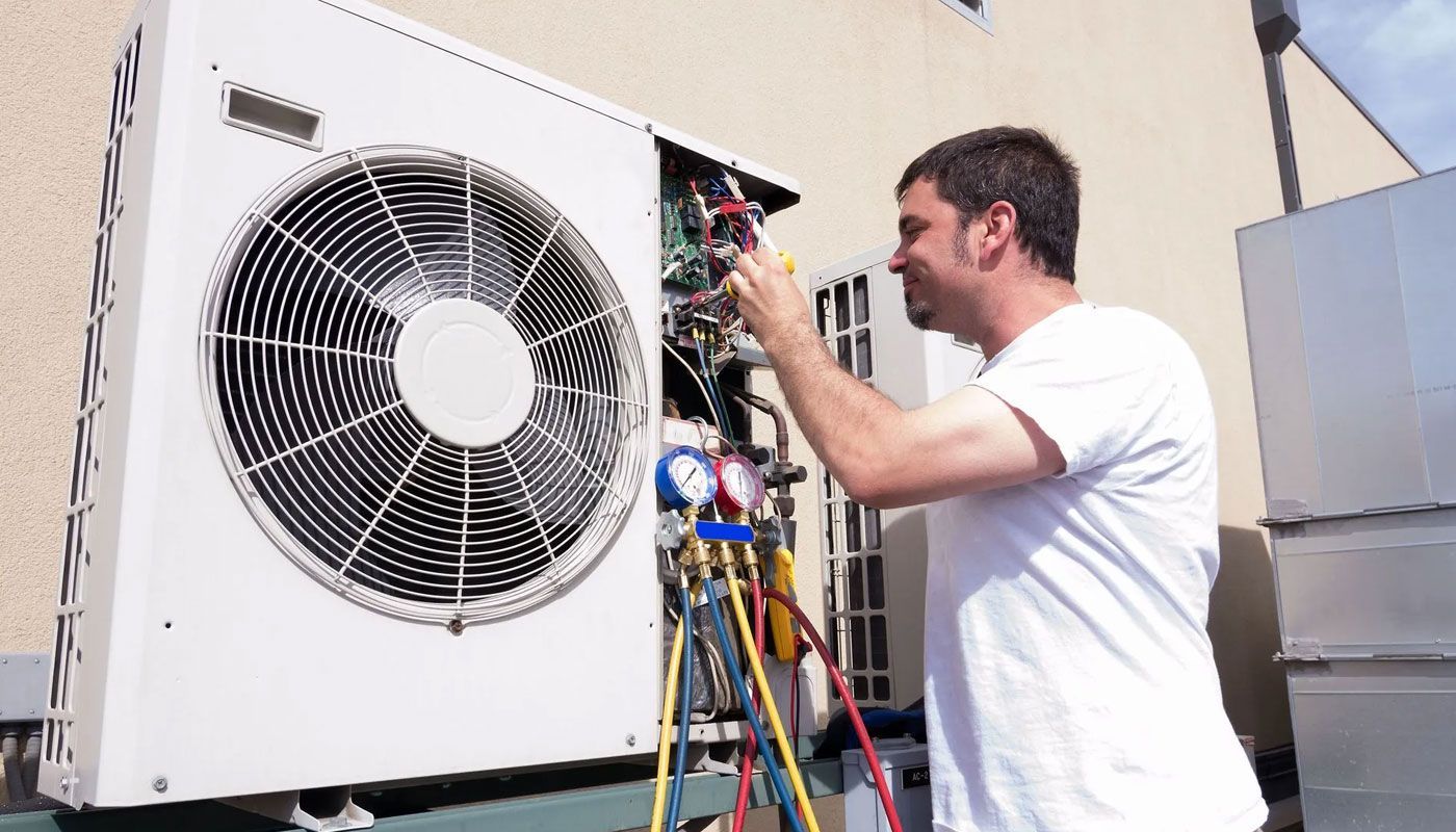 Technician repairing an outdoor HVAC unit with exposed wires and tools attached.