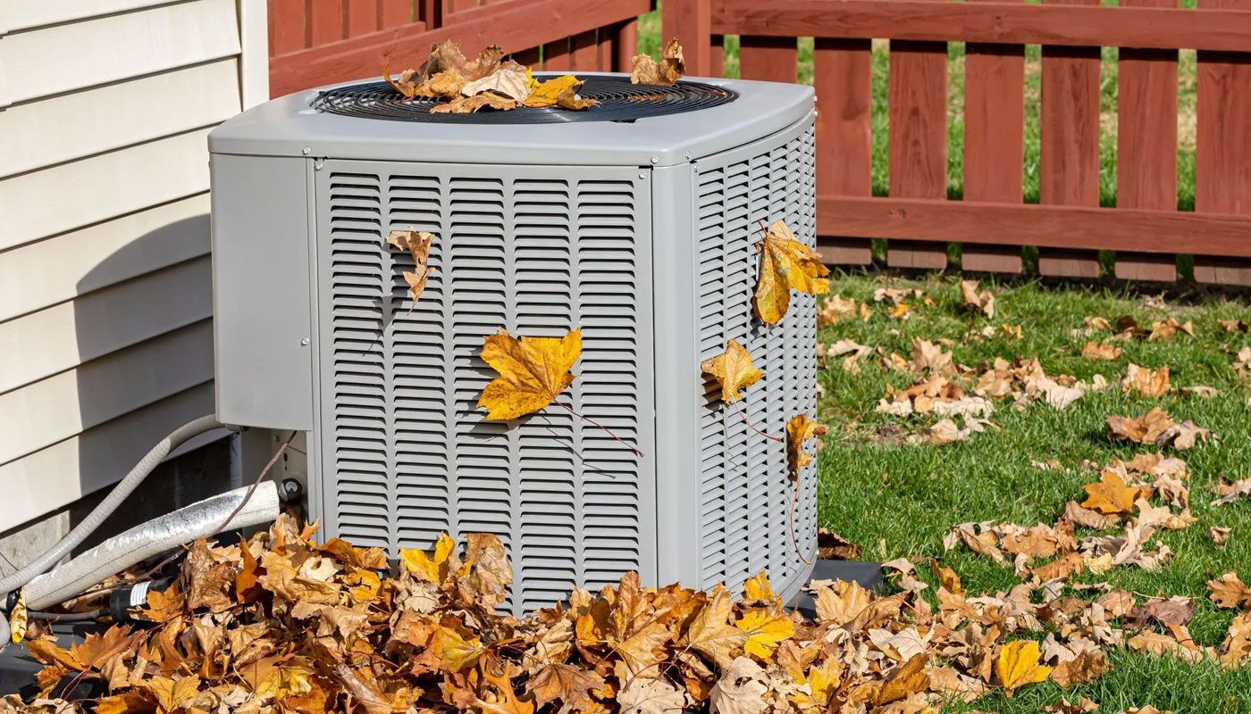 Air conditioner unit beside a house, surrounded by fallen autumn leaves in a yard