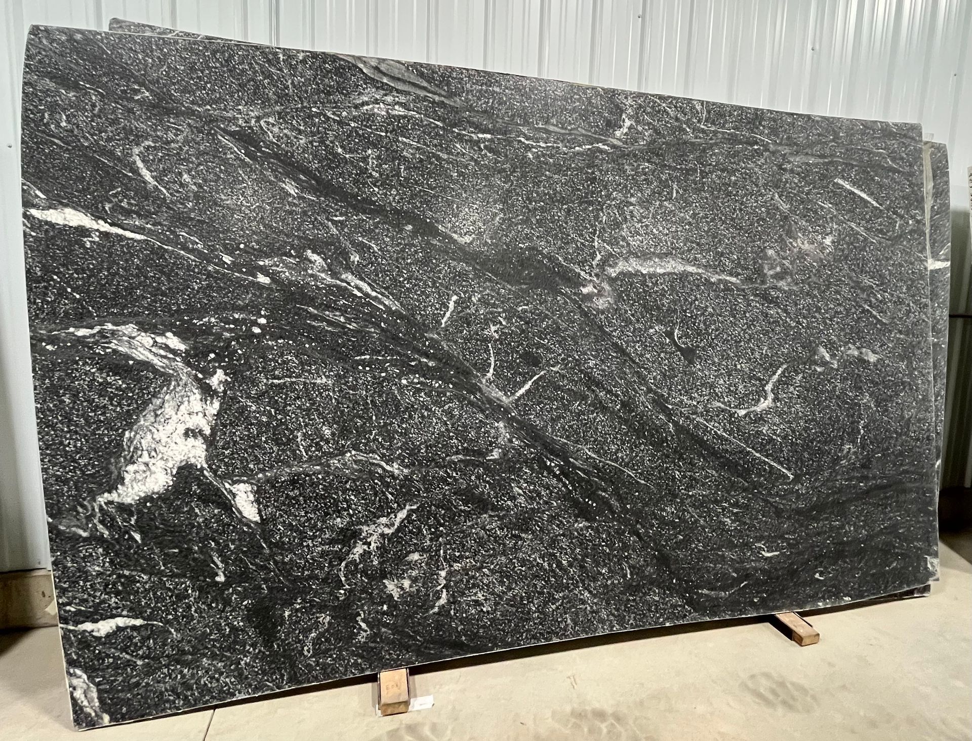 A large black granite slab is sitting on top of a cement floor.