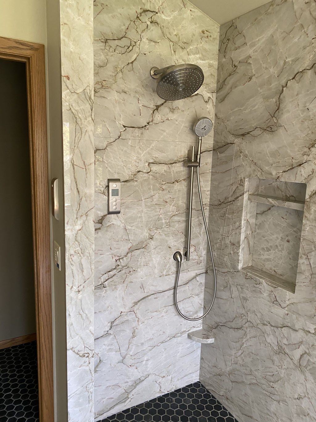 A shower with marble walls and a stainless steel shower head.