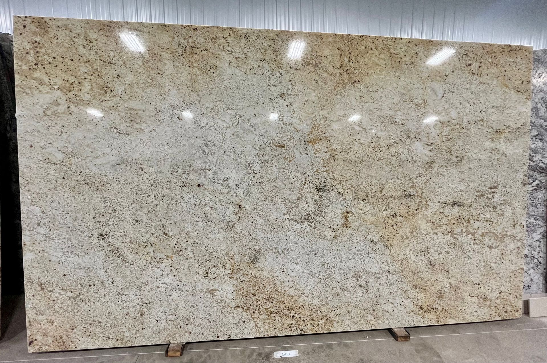Large beige speckled granite slab standing upright in a warehouse or stone yard.