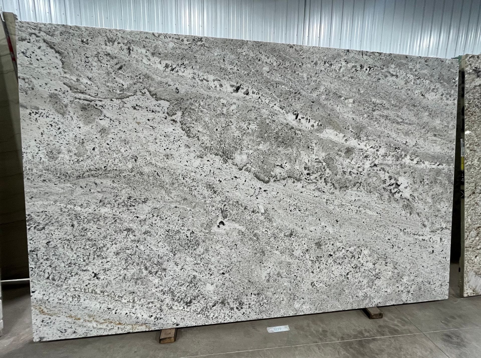 Large speckled gray granite slab standing upright in an industrial warehouse setting