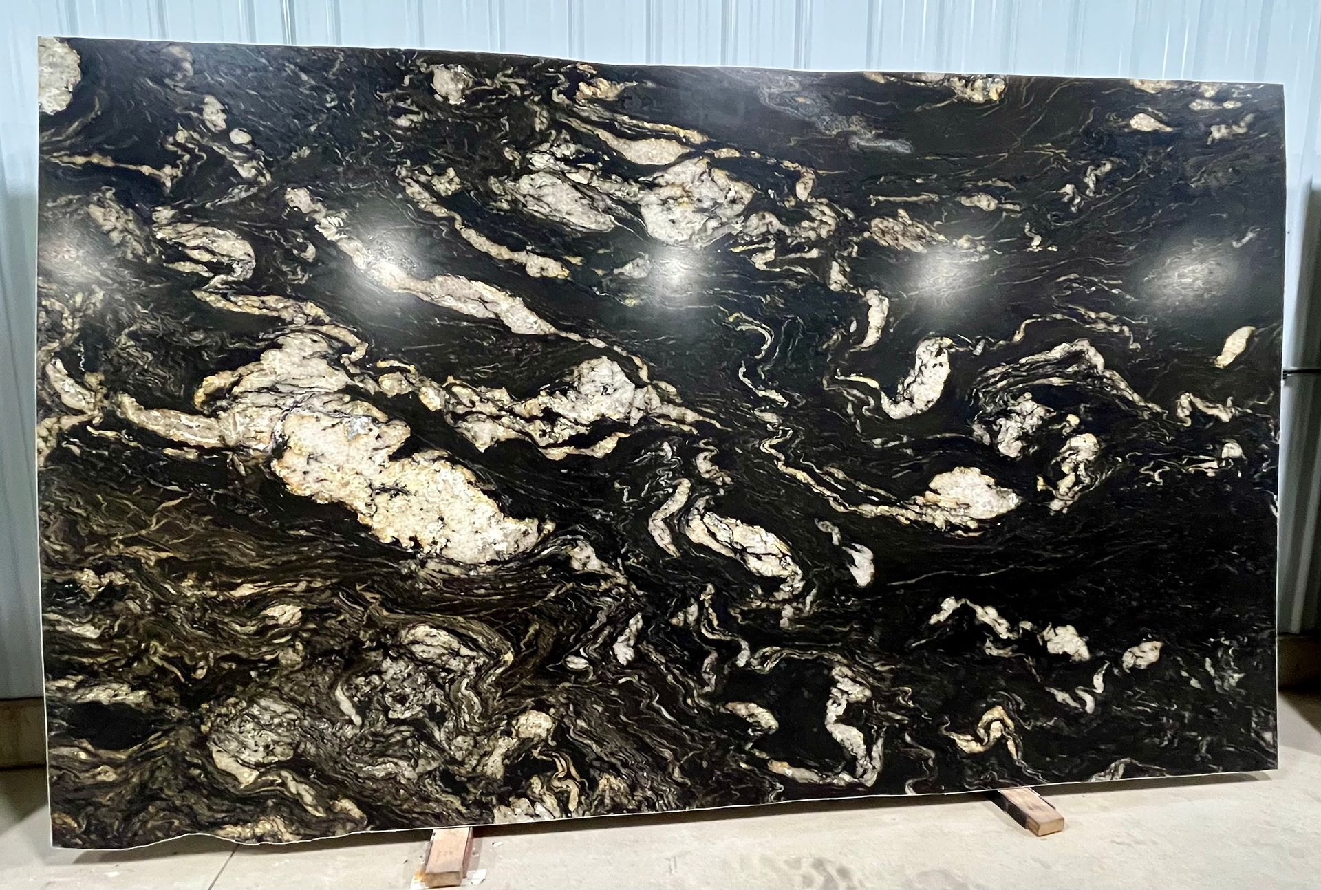 Large polished black stone slab with white and gold veining, displayed on stands in a showroom