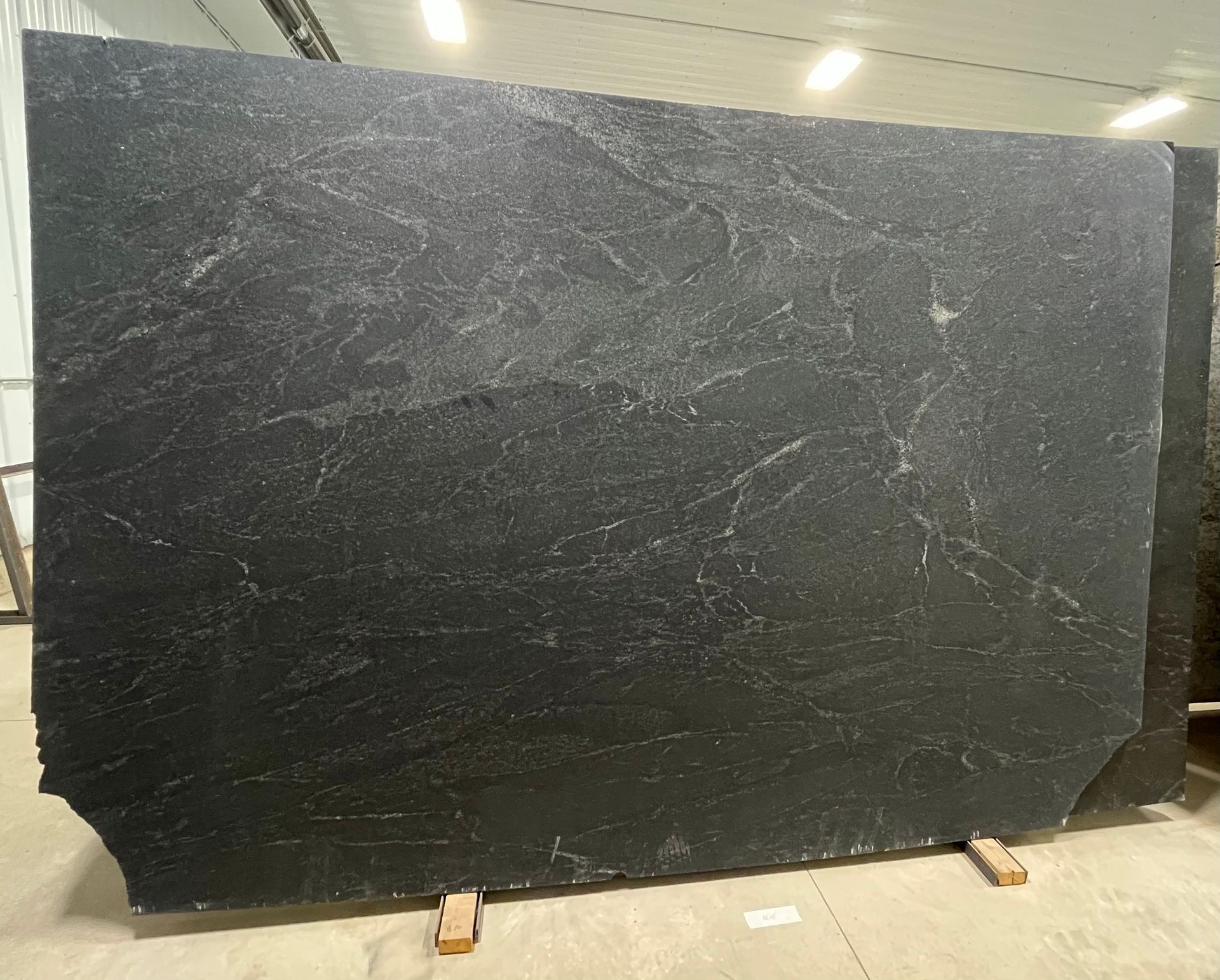 A large, rectangular slab of dark black granite with subtle, light-colored veining, displayed on a wooden stand.