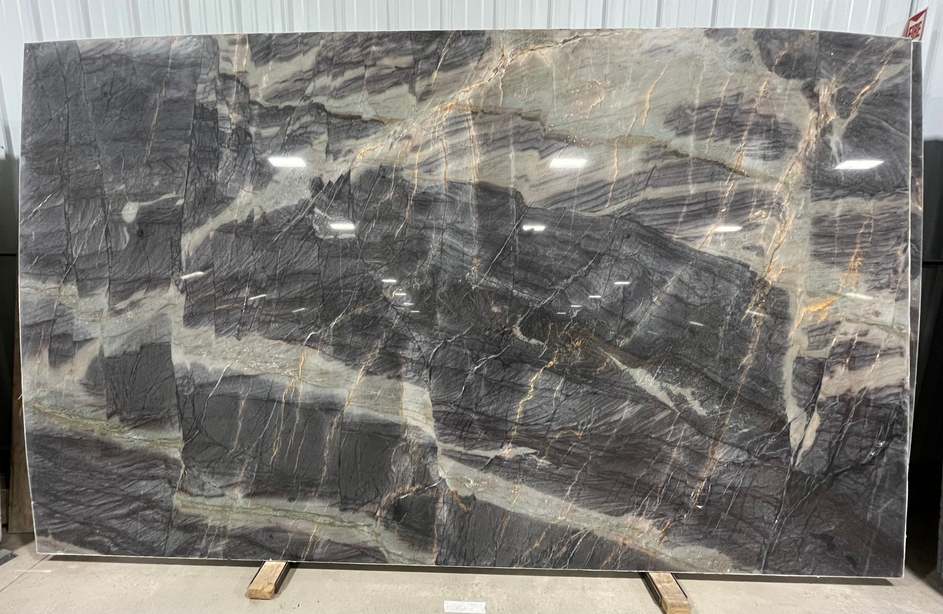 A large, polished stone slab with dark gray and black veining accented by streaks of white, beige, and copper-brown.