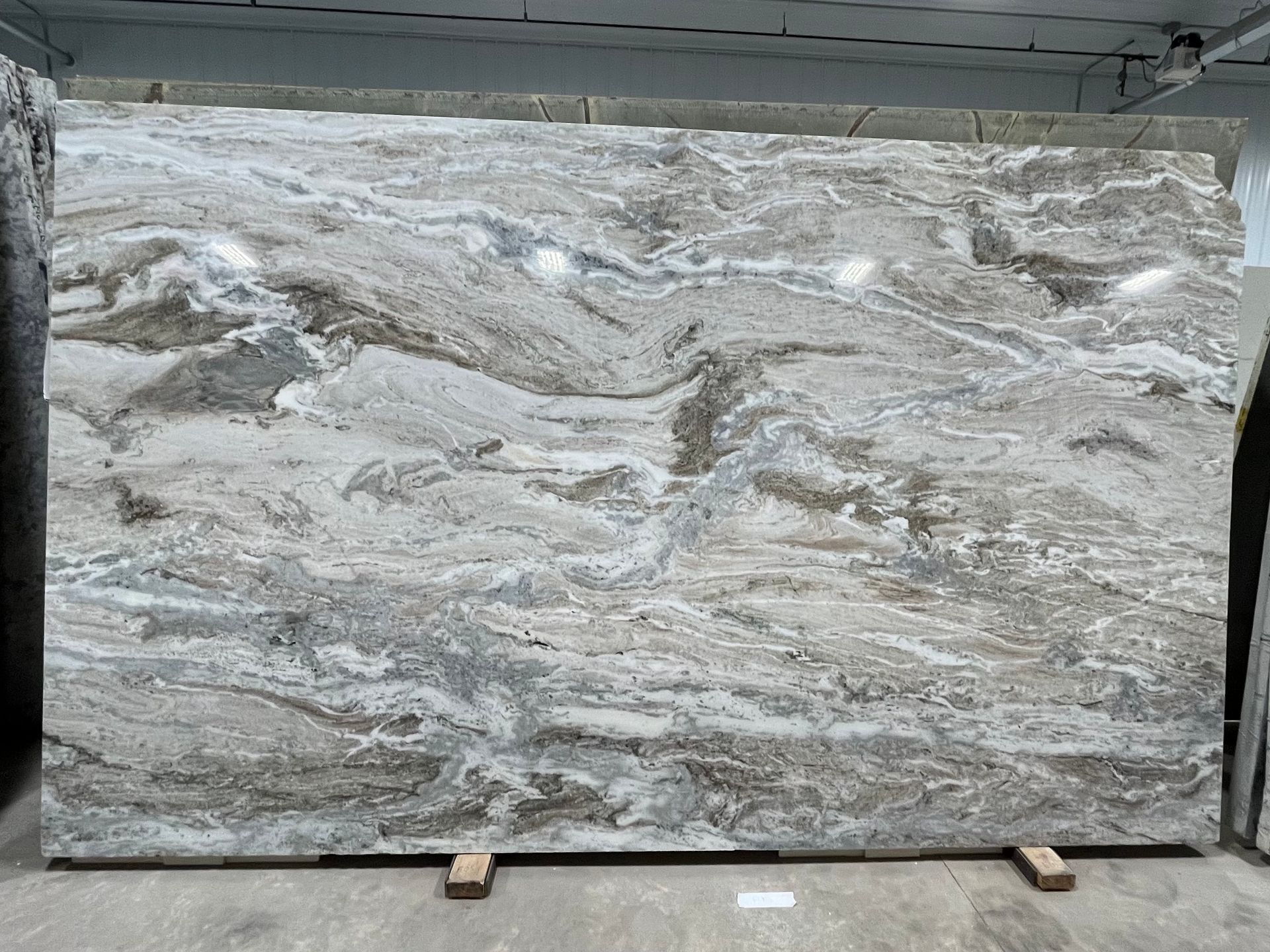 Large slab of polished marble with swirling, flowing patterns of white, cream, gray, and dark brown earth tones.